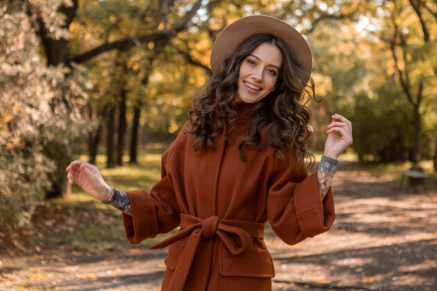 漂亮迷人时尚微笑的瘦身女子卷发漫步公园身着暖棕色外套 秋日时尚街头风配饰苗条时尚