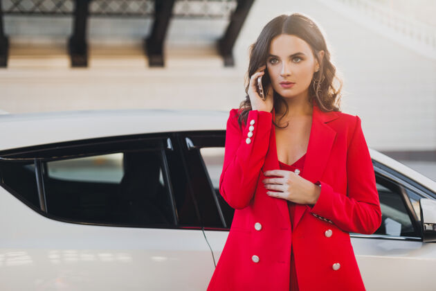 年轻穿着红西装的性感美女在车前摆姿势打电话谈生意优雅女人穿着