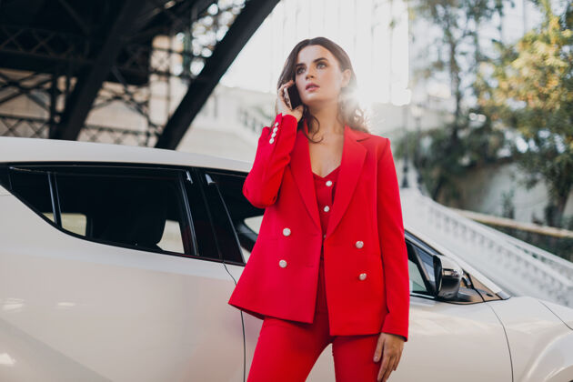 年轻穿着红西装的性感美女在车前摆姿势打电话谈生意汽车通话智能手机