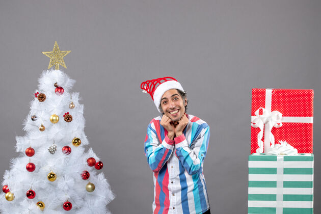 微笑前视图快乐帅哥把手放在他的脸上靠近白色圣诞树微笑灰色快乐