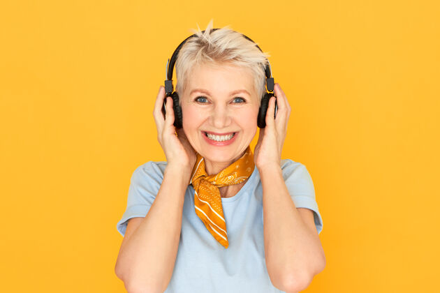 成人快乐快乐的成熟短发女人 戴着无线耳机 在黄色的脸上微笑着肖像老年人耳机