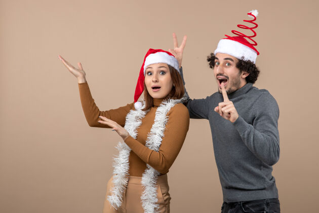 指向圣诞节心情激动凉爽满意可爱情侣戴着红色圣诞老人帽指着上方帽子可爱酷