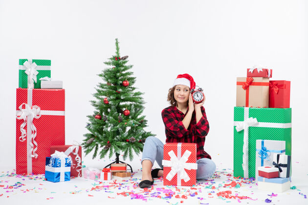 礼物前视图的年轻女子坐在圣诞礼物周围拿着白色墙上的时钟人礼物十二月