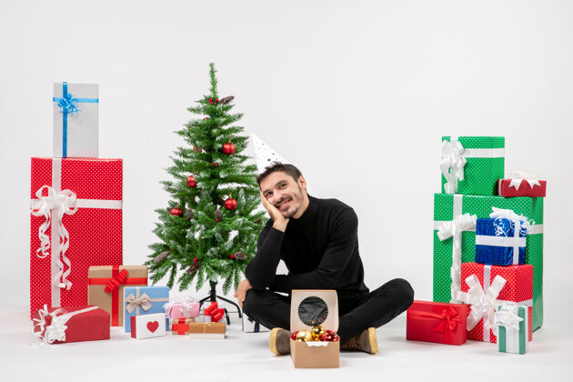 坐着年轻人坐在白色墙上的节日礼物周围的正面视图十二月雪成人