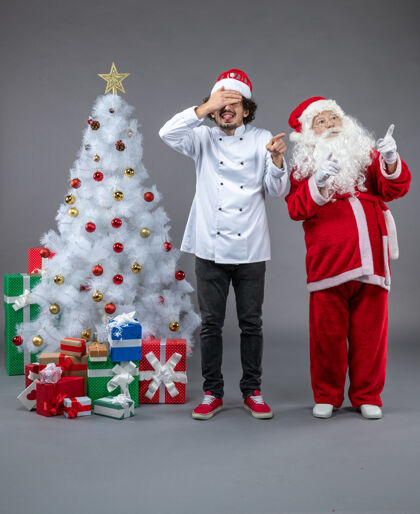 前面圣诞老人和男厨师在灰色墙上围着圣诞礼物的正视图服装圣诞老人礼物