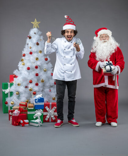圣诞老人圣诞老人和男厨师在灰色墙上围着圣诞礼物的正视图礼物前面圣诞老人