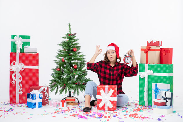 人前视图的年轻女子坐在圣诞礼物周围拿着白色墙上的时钟礼物坐着圣诞