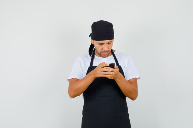 黑板面包师穿着t恤 围着围裙用手机 看上去很忙工人成人围裙