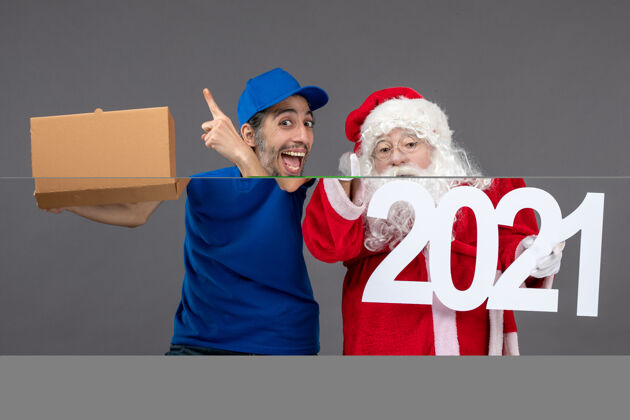 圣诞老人圣诞老人的正面图 男信使拿着食物盒 在灰色的墙上写字帽子快乐圣诞快乐