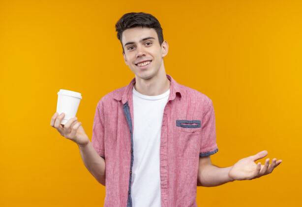小伙子笑容满面的白人年轻人穿着粉色衬衫 手举咖啡杯 背景是孤立的橙色抱着咖啡橙色
