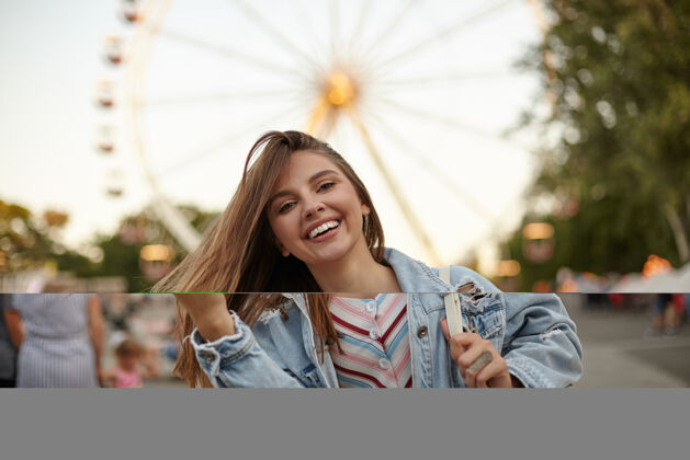 城市迷人的棕色长发少女 穿着休闲服 在摩天轮上摆姿势 挥舞着头发 愉快地微笑 积极的情感概念背包公园休闲