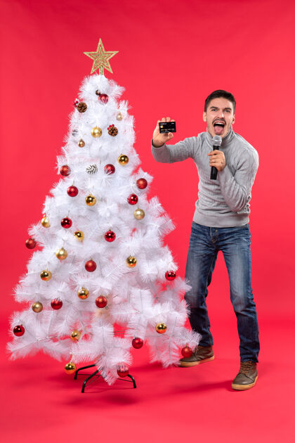 树圣诞节心情与情绪化的家伙站在装饰圣诞树附近 手持麦克风和电话唱歌快乐电话情绪家伙