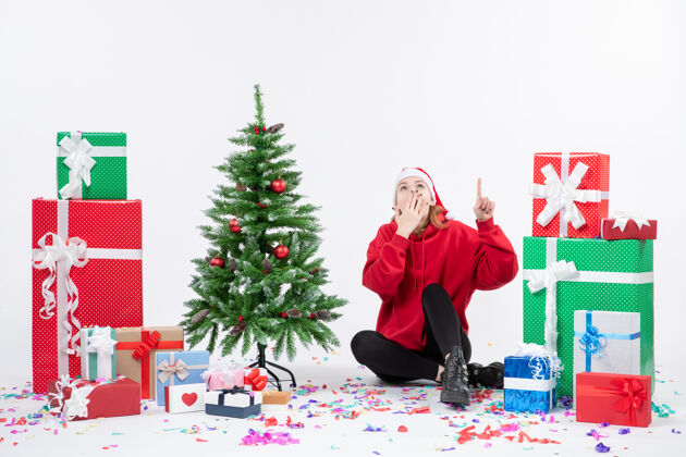 礼物年轻女子坐在白色墙壁上的节日礼物周围的正面视图节日情感树