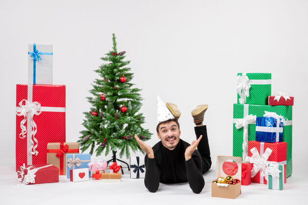 冬天年轻人躺在白色墙上的节日礼物周围的正面视图帽子人装饰