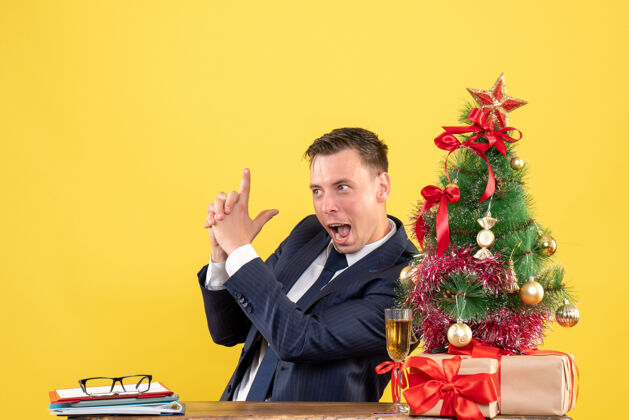 制作一个年轻人坐在圣诞树旁的桌子旁 手里拿着一把 手里拿着黄色的礼物男人礼物年轻人