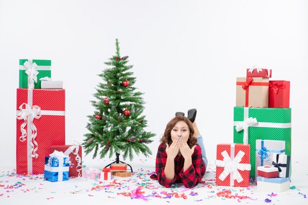 树正面图年轻女性躺在白色地板上的圣诞礼物和圣诞树周围圣诞新年礼物颜色雪地礼物女年轻的女性