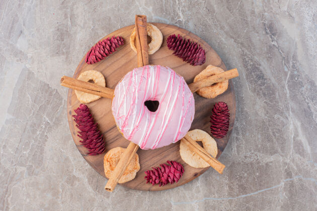 圆锥体肉桂棒和干苹果片围绕着一个甜甜圈放在一块松果装饰的大理石板上曲奇美味视图