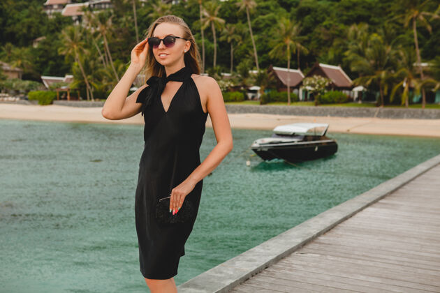 海洋奢华性感迷人的女人穿着黑色礼服在豪华度假酒店的码头上摆造型 戴着墨镜 暑假 热带海滩码头女人优雅