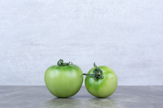 植物两个绿色的西红柿放在大理石桌上叶子番茄有机