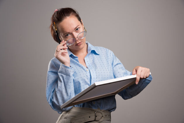 眼镜戴眼镜的女人拿着帆布 在灰色背景上画笔高质量的照片绘画持有设备