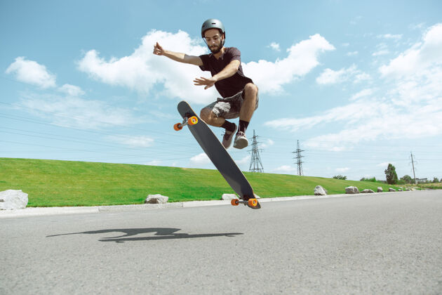 极限在阳光明媚的日子里 在城市街道上玩滑板的人年轻人在草地附近骑马 玩长板休闲活动 运动 极限 爱好和运动的概念年轻人户外运动