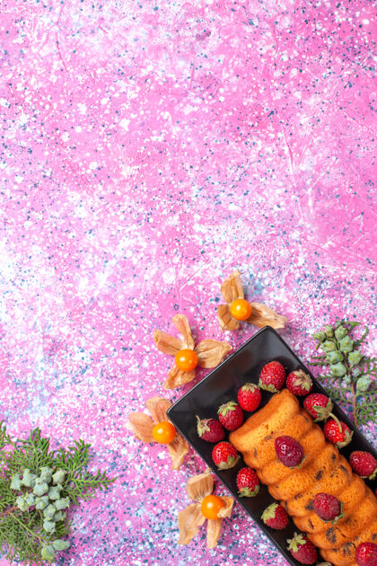 草莓顶视图美味的蛋糕在黑色的蛋糕锅里 粉红色的桌子上放着新鲜的红色草莓植物顶部烘焙