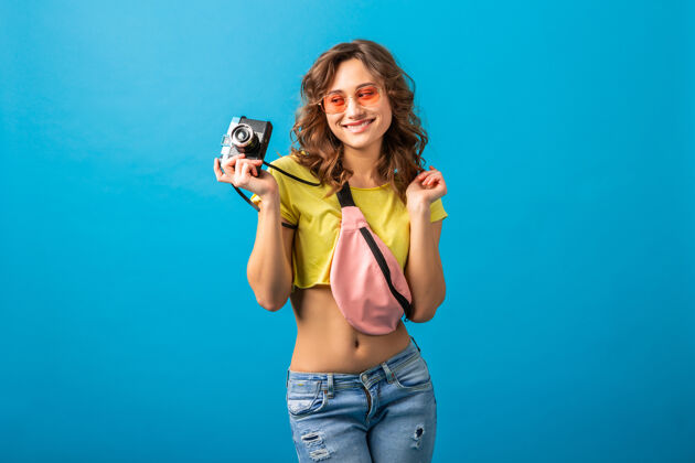 肖像迷人的微笑快乐的女人摆姿势与老式相机拍照穿着时髦的夏季五颜六色服装隔离在蓝色工作室的背景蓝色休闲相机