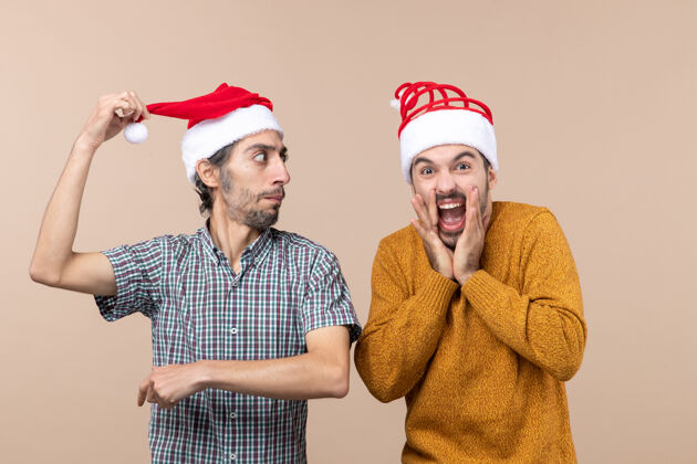 前面前视图两个家伙一个拿着圣诞帽另一个在米色背景下大声喊叫成人伙计们风景