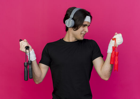 做一个穿着运动服 头戴耳机 手拿两根跳绳的年轻人看起来很困惑 正试图做出选择绳子耳机运动