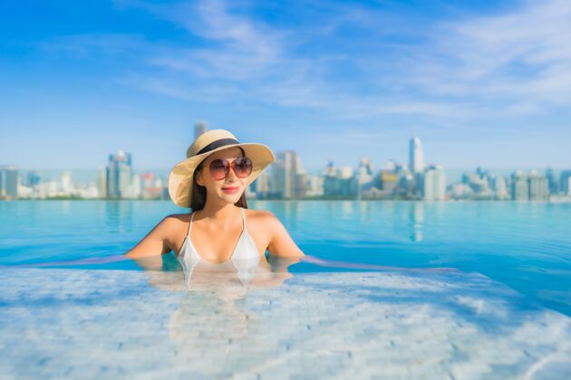 度假村美丽的亚洲年轻女子在户外游泳池周围放松 城市景色尽收眼底水豪华高