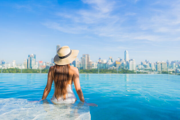 高美丽的亚洲年轻女子在户外游泳池周围放松 城市景色尽收眼底城市比基尼豪华