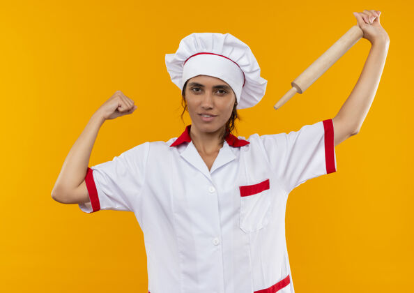 厨师高兴的年轻女厨师穿着厨师制服 肩上举着擀面杖做着坚强的手势高兴滚强壮