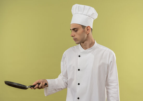 平底锅想着年轻的男厨师穿着厨师制服看着手中的炒锅 手拿抄写空间煎穿男
