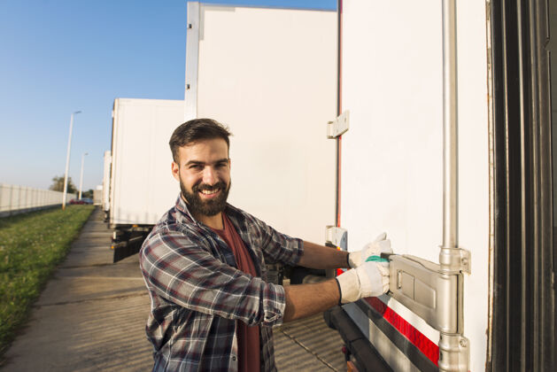运输微笑着戴着工作手套的卡车司机打开或关闭卡车拖车后门检查货物运输货运航运公路