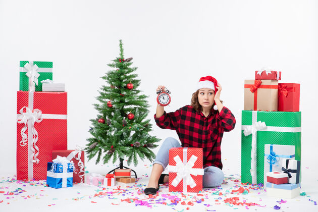 十二月前视图的年轻女子坐在圣诞礼物周围拿着白色墙上的时钟庆祝快乐礼物