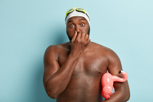 强壮惊讶的非洲裔美国男子捂着鼻子 在潜水前屏住呼吸 腋下夹着游泳圈的照片种族水平运动