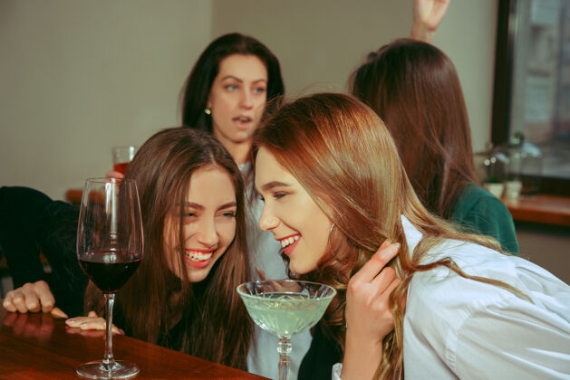 漂亮女朋友在酒吧喝酒她们坐在一张有鸡尾酒的木桌旁手聚会食物