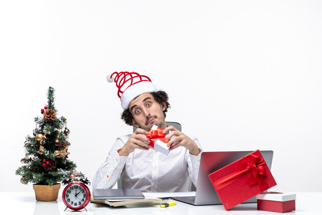 礼物圣诞节心情惊讶的商人和圣诞老人的帽子举起他的礼物 看着它在白色的背景生活礼物圣诞老人