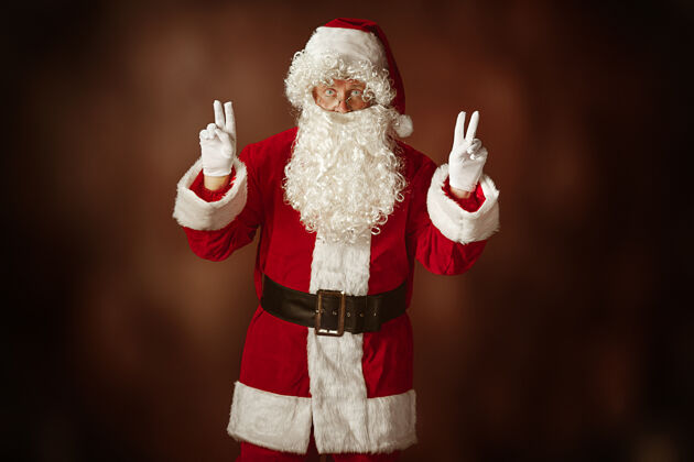 场合穿着圣诞老人服装的人的肖像-一个豪华的白胡子 圣诞老人的帽子和红色的服装在红色工作室的背景老年人欢乐圣诞节