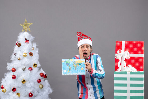旅行者前视图困惑的男子螺旋弹簧圣诞帽和条纹衬衫举行地图把他的手放在脸上旅行家伙庆祝