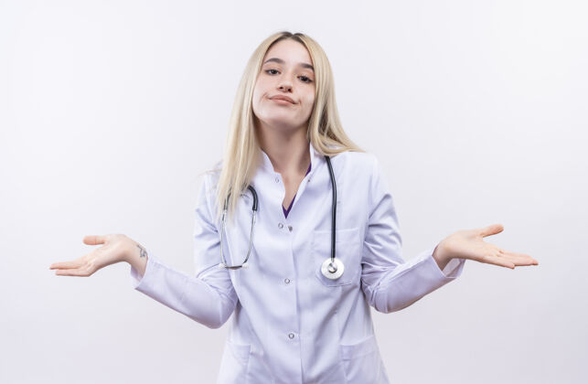 手势微笑的医生年轻的金发女孩戴着听诊器和医用长袍在孤立的白色背景上显示什么姿势穿着医生年轻
