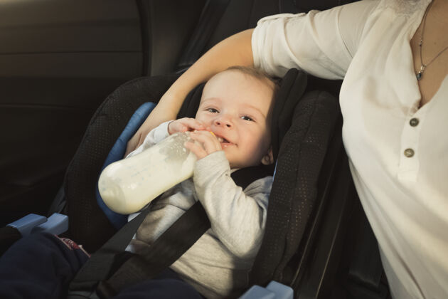 旅程可爱的男婴拿着奶瓶坐在汽车座椅上的画像安全紧固件团结