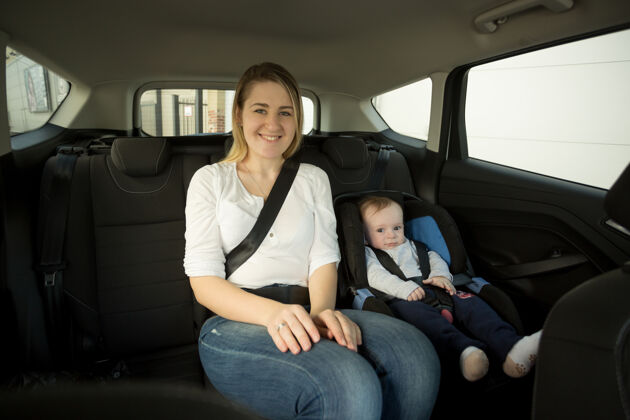 女人快乐微笑的母亲和她的孩子在后座上的画像护理旅行车辆
