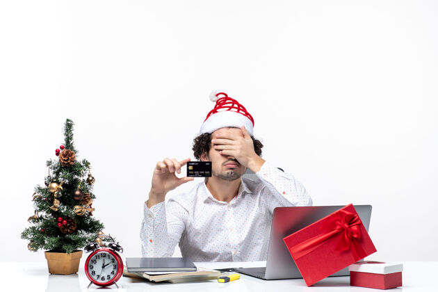 银行在白色背景的办公室里 戴着圣诞老人帽 拿着银行卡的年轻疲惫的商务人士带着节日的喜庆心情商务年轻人圣诞节