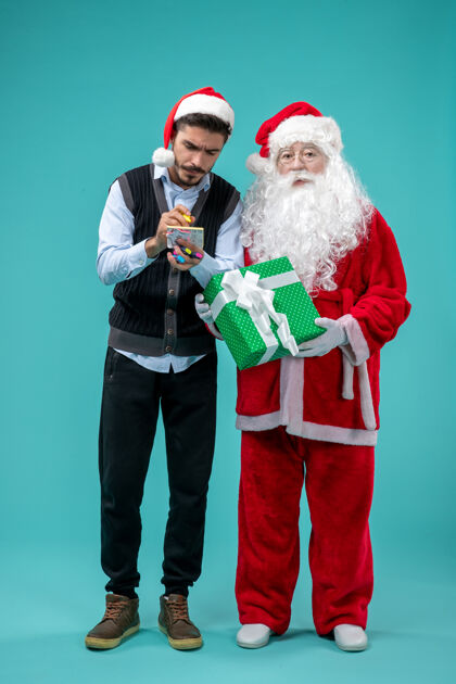 年轻前视图：圣诞老人和正在蓝色背景上做笔记的年轻男性笔记采取圣诞老人
