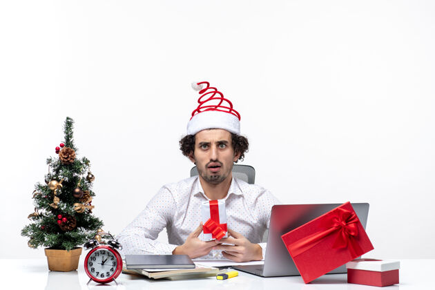微笑圣诞节心情与震惊的年轻商人圣诞老人帽子和举行他的礼物头脑风暴在白色背景年轻圣诞老人帽子