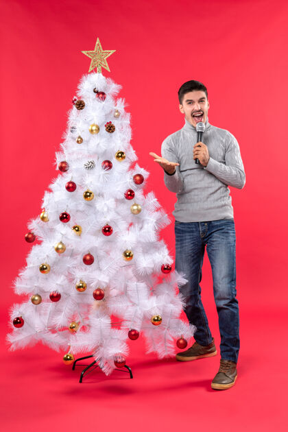 呼叫圣诞节心情积极的家伙穿着牛仔裤站在装饰圣诞树附近打电话给某人站着圣诞树红色