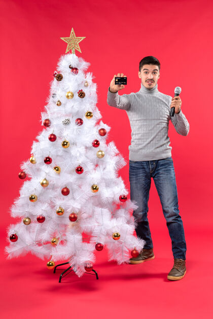 站着圣诞气氛 年轻人站在装饰好的圣诞树旁 拿着麦克风 拿着手机圣诞树展示抱着