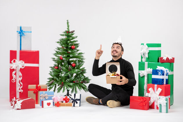 礼物正面图：年轻人围坐在节日礼物旁边 手里拿着白色墙上的玩具包包装情感雪