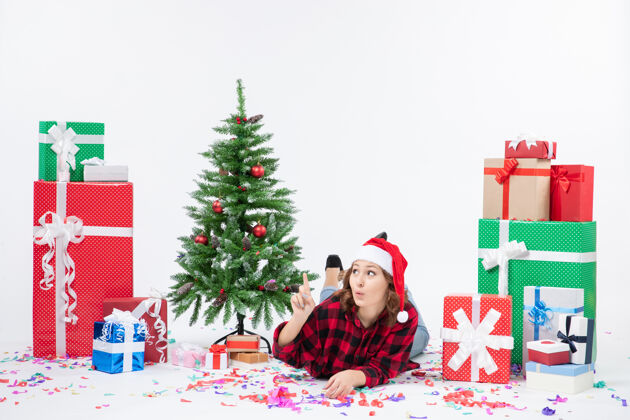 周围前视图年轻女性躺在圣诞礼物和小圣诞树周围 背景颜色为白色 新年妇女圣诞雪小礼物雪